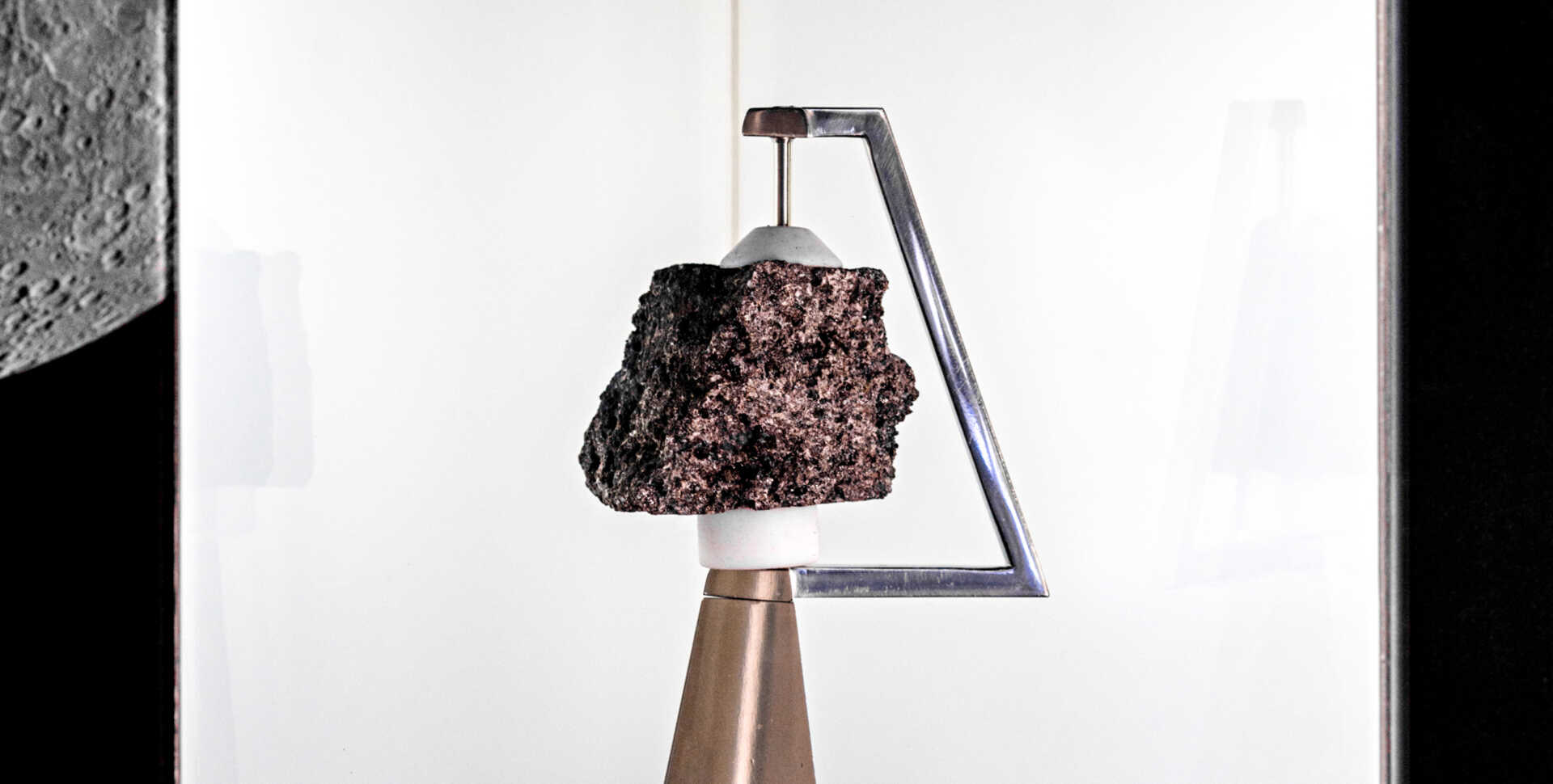The moon rock is displayed in its container, held up by a metal arm and pedestal.