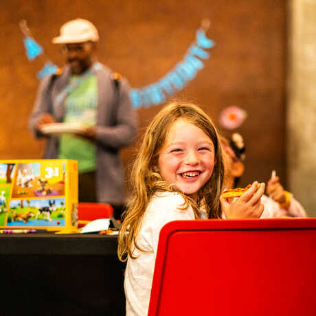 Grinning young girl with a mouthful of cookie at a birthday party hosted by Cal Academy