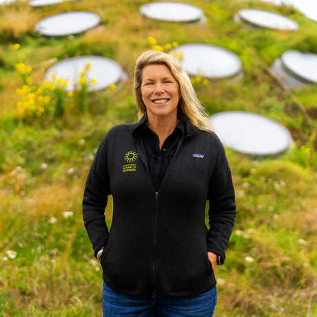 Shannon Tushingham stands with arms in her pockets on the Living Roof, against one of the window-dotted grassy mounds. 